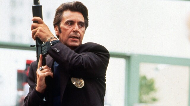 alt="Al Pacino holding a rifle while wearing a dark suit in Heat, 1995 crime drama also starring Val Kilmer."