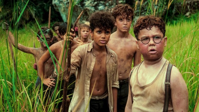 a group of disheveled boys holding walking sticks in a field of grass
