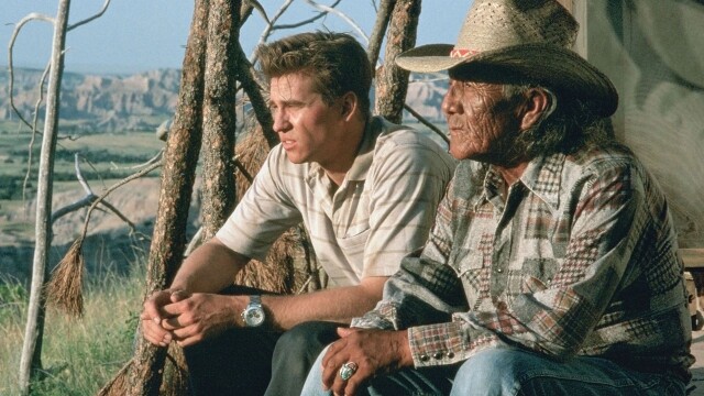 alt="Val Kilmer in Thunderheart, 1992 crime drama, sitting outdoors with a Native American elder against a scenic landscape"